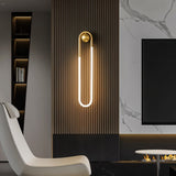 "A modern, minimalist U-shaped wall lamp with a brass finish illuminating a living room with a marble accent wall."