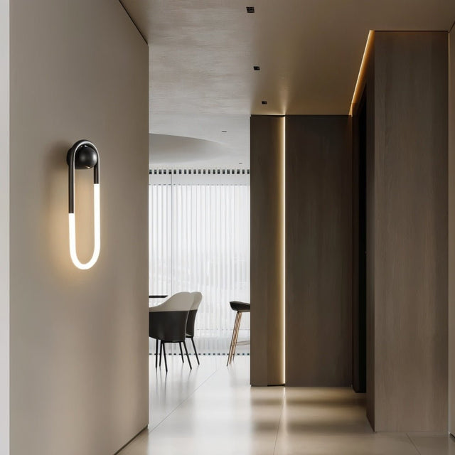 "A modern, minimalist U-shaped wall lamp with a black and brass finish illuminating a hallway."