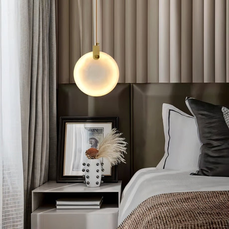 "A modern alabaster pendant light hangs above a nightstand in a contemporary bedroom, casting a warm glow."
