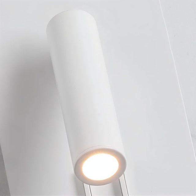 "Close-up of a modern white cylindrical spotlight emitting a focused beam of light, part of a wall-mounted reading lamp."