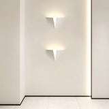 "Two lit white trimless wall lights with a geometric design on a white wall in a modern hallway."