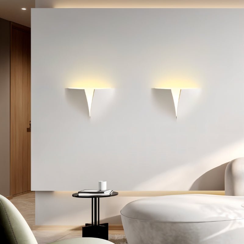 "Two lit white trimless wall lights with a geometric design on a white wall in a modern living room setting."