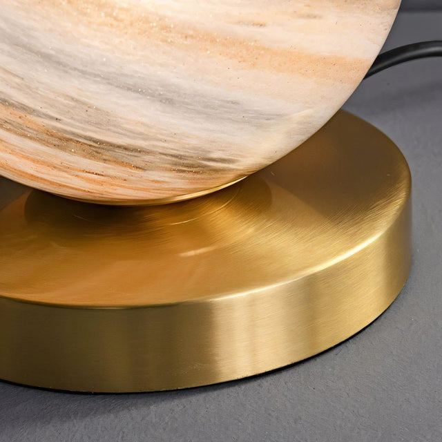 "Close-up of a modern table lamp with brass base and marble glass globe shade, showing the base's detail."