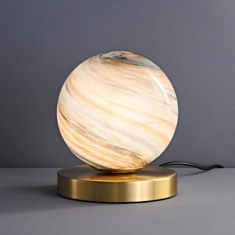 "Modern table lamp with marble glass globe shade and brass base, emitting a soft ambient glow."