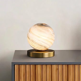 "Modern table lamp with marble glass globe shade and brass base, emitting a soft ambient glow."