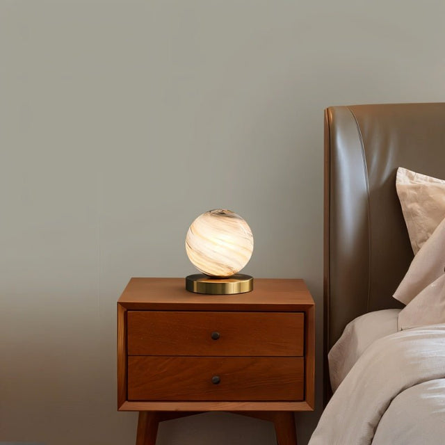 "Modern table lamp with marble glass globe shade on a wooden nightstand, illuminating a bedroom."