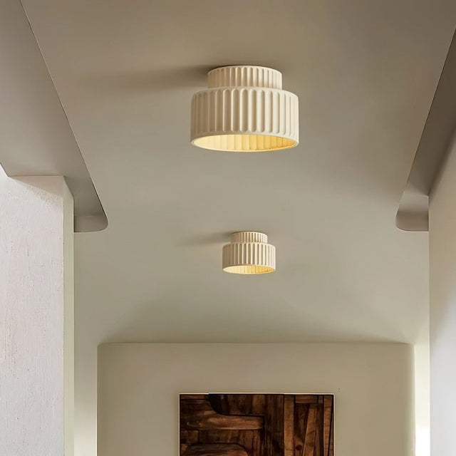 "Two beige ceiling lights with ribbed shades and gold interiors, shown installed on a white ceiling in a hallway with a framed painting."