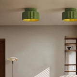 "Two green ceiling lights with ribbed shades and gold interiors, shown installed on a white ceiling in a living room with a floor lamp and a shelving unit."