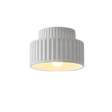 "A white ceiling light with a ribbed, cylindrical shade, shown lit up against a white background."