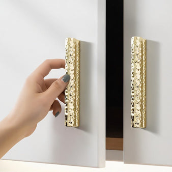 "Gold hammered texture pull bar handles on white cabinet doors, showcasing a modern and handcrafted aesthetic."