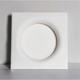 "A square white ceiling light with a round, recessed center, against a light gray background."