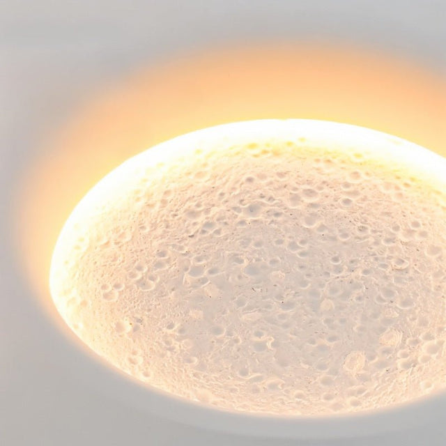 "A round, recessed wall light casting a warm, lunar-like glow on a wall above a couch in a modern living room."