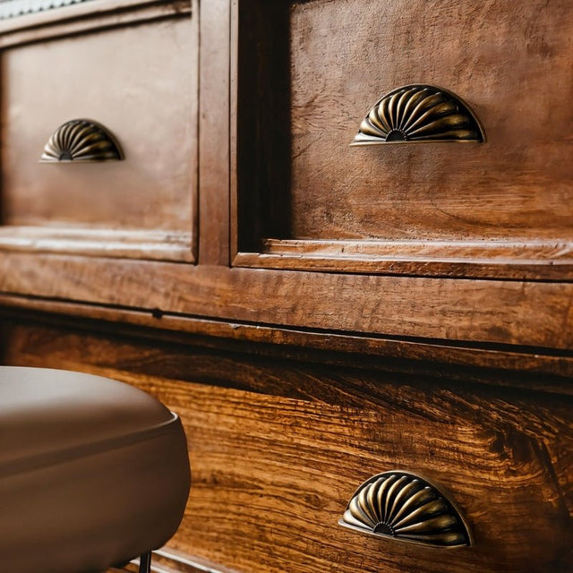 "Vintage brass fan-shaped drawer pulls with detailed ridges and a black undertone, installed on a traditional wooden dresser, enhancing its antique style."