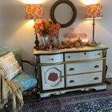 "Vintage brass fan-shaped drawer pulls with detailed ridges, installed on a painted dresser in a traditionally decorated room with lamps and a round mirror."