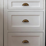 "Vintage brass fan-shaped drawer pulls with detailed ridges, installed on a white dresser, enhancing its traditional style."