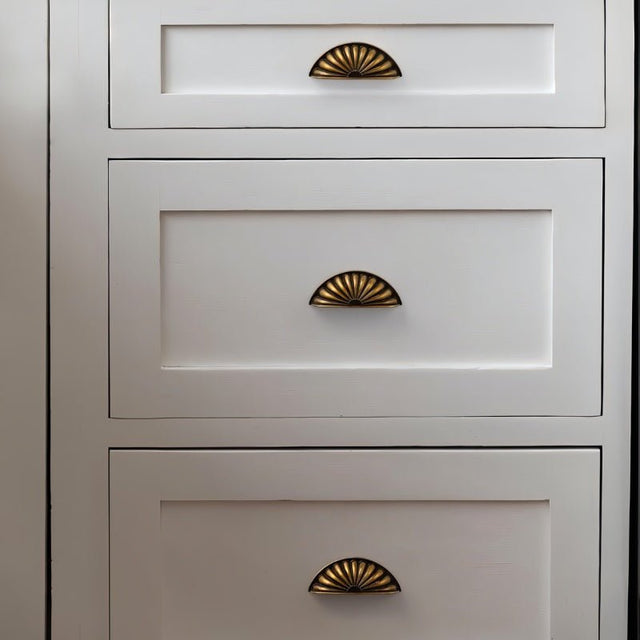 "Vintage brass fan-shaped drawer pulls with detailed ridges, installed on a white dresser, enhancing its traditional style."