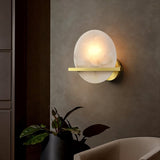 "Round alabaster wall lamp with brass frame, emitting a soft, diffused light on a dark wall."