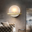 "Round alabaster wall lamp with brass bar, illuminating a living room with a soft, ambient light."