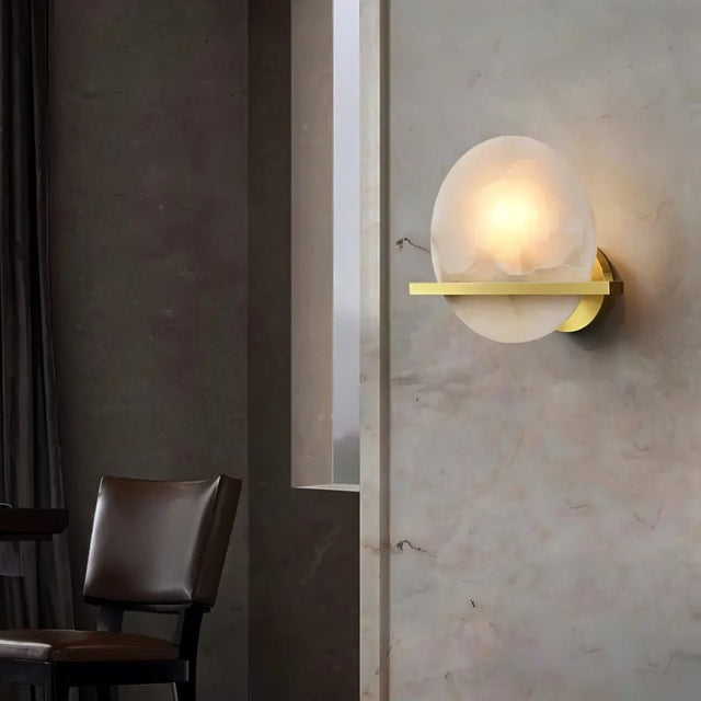 "Round alabaster wall lamp with brass accents, illuminating a modern living room with a soft glow."