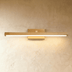 Wooden linear vanity light fixture above round mirror on herringbone tile wall, warm brass finish, studio setting.