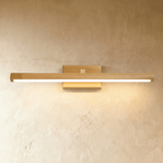 Wooden linear vanity light fixture above round mirror on herringbone tile wall, warm brass finish, studio setting.
