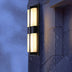 Vertical alabaster wall sconce with black metal frame mounted on wet exterior wall at dusk.