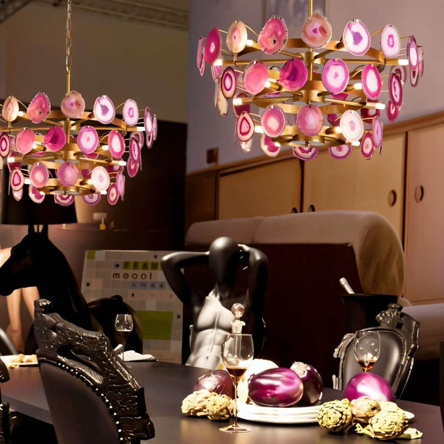 "Two gold metal Zylan chandeliers with layered circular design and pink agate slices, hanging above a dining table with a mannequin."
