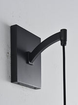 "Close-up detail of a modern black wall lamp, showcasing its rectangular base and curved arm, blending elegance and minimalist design."