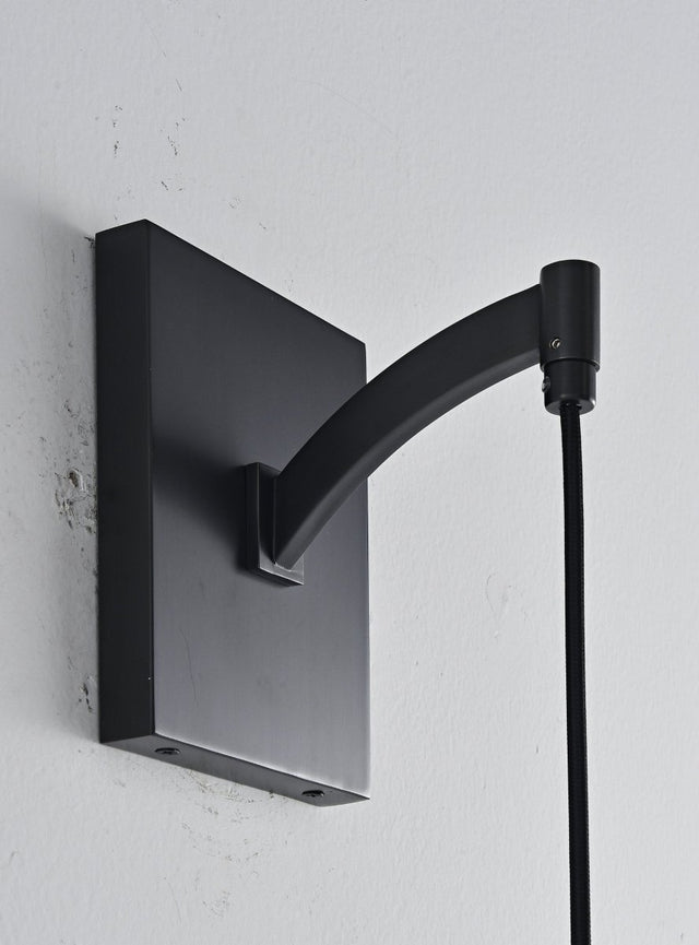 "Close-up detail of a modern black wall lamp, showcasing its rectangular base and curved arm, blending elegance and minimalist design."