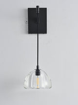 "A modern black wall lamp with a clear glass shade, blending elegance and minimalist design with a curved arm and rectangular base."