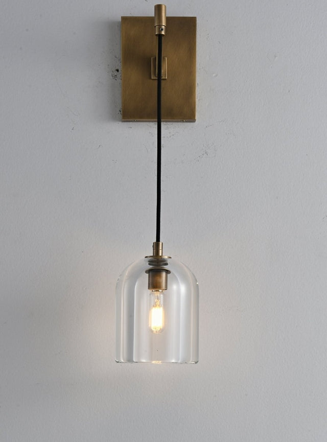 "A modern brass wall lamp with a dome-shaped clear glass shade, blending elegance and minimalist design with a curved arm and rectangular base."