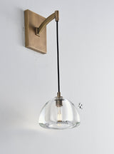 "A modern brass wall lamp with a dome-shaped clear glass shade, blending elegance and minimalist design with a curved arm and rectangular base."