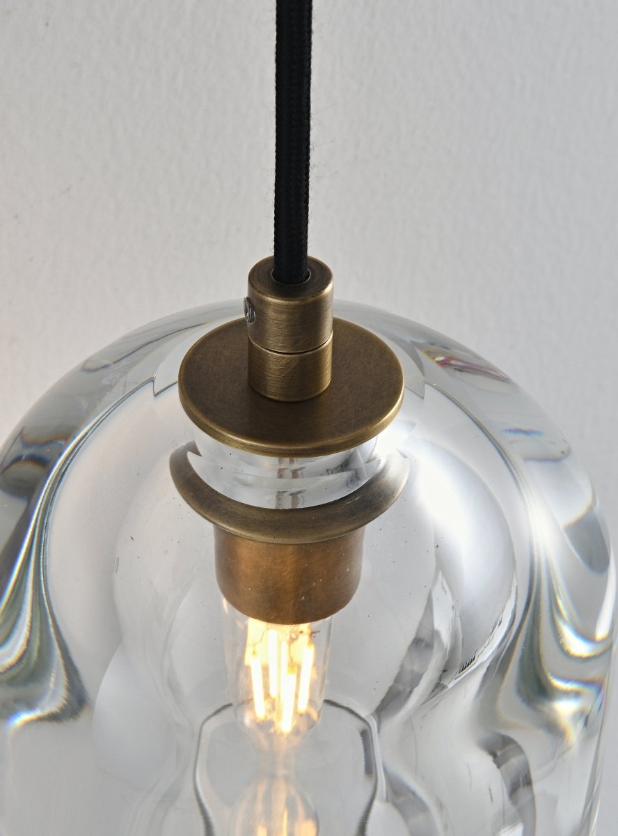  "Close-up detail of a modern glass wall lamp with a clear shade, showing the brass fixture and illuminated bulb."