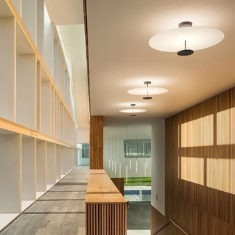 "Multiple minimalist ceiling lights with circular acrylic diffusers and sleek metal frames lining a modern office hallway."