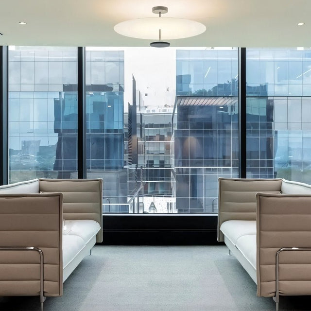 "A minimalist ceiling light with a circular acrylic diffuser and a sleek metal frame in a modern office space with large windows."