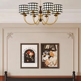 "A six-light chandelier with black polka dot shades hangs above a bed in a bedroom with framed art on the wall."