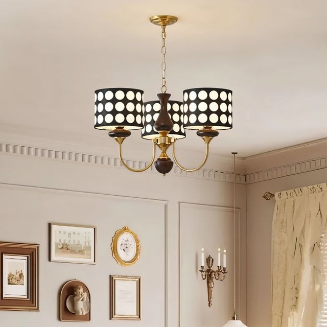 "A three-light chandelier with black polka dot shades hangs above a dining table in a modern dining room."