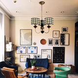 "A three-light chandelier with black polka dot shades hangs in a mid-century modern living room with art and furniture."