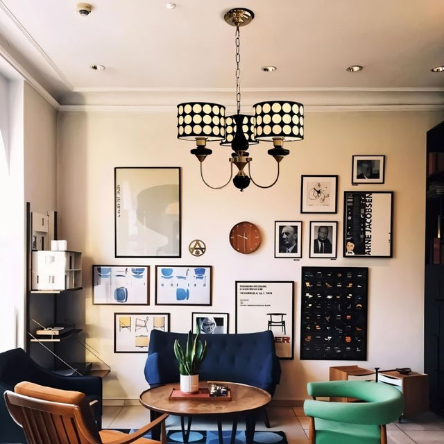 "A three-light chandelier with black polka dot shades hangs in a mid-century modern living room with art and furniture."
