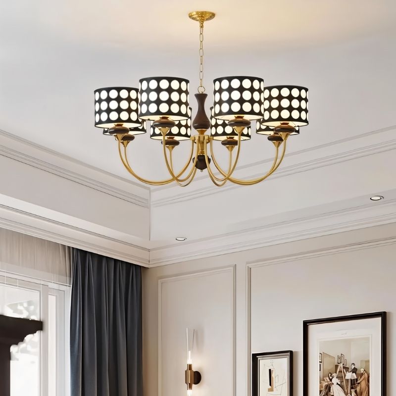 "A six-light chandelier with black polka dot shades hangs in a living room with high ceilings and large windows."