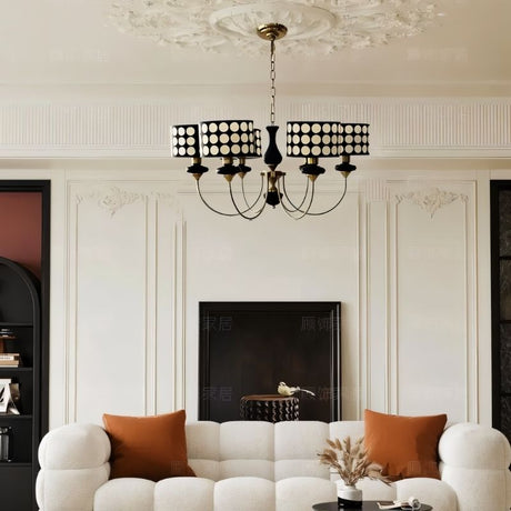 "A six-light chandelier with black polka dot shades hangs above a white sofa in a classically decorated living room."