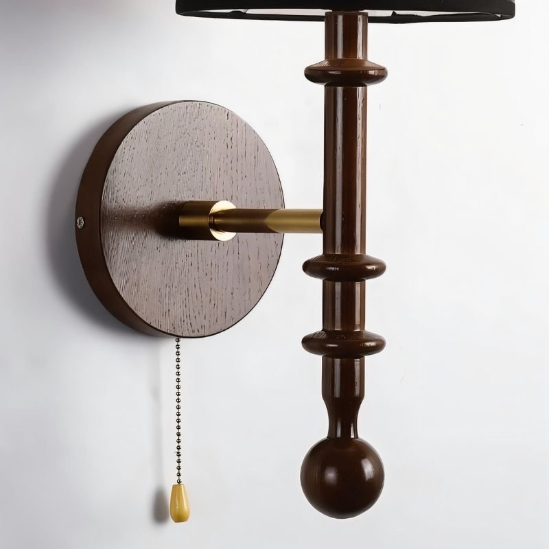 "A walnut and gold wall lamp with a black shade and pull chain, installed on a white wall."