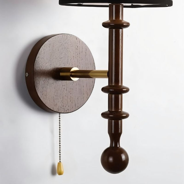 "A walnut and gold wall lamp with a black shade and pull chain, installed on a white wall."