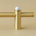 Brass pull bar with marble sphere finial on neutral beige background.