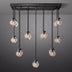 Black metal linear chandelier with nine ribbed glass globe pendants hanging at varying heights against a gray background.