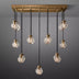 Linear chandelier with brass fixture and eight ribbed glass globe pendants against gray background.