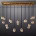 Linear chandelier with brass canopy and 16 ribbed glass globe pendants suspended by black cords against a gray background.