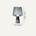 Modern table lamp with smoky gray glass shade and dark cone base on neutral background.