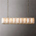 Linear chandelier with brass finish and stacked alabaster stone panels suspended by chains against a gray wall.