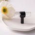 Clear glass spray atomizer with black band and handle displayed on white surface next to white flower.